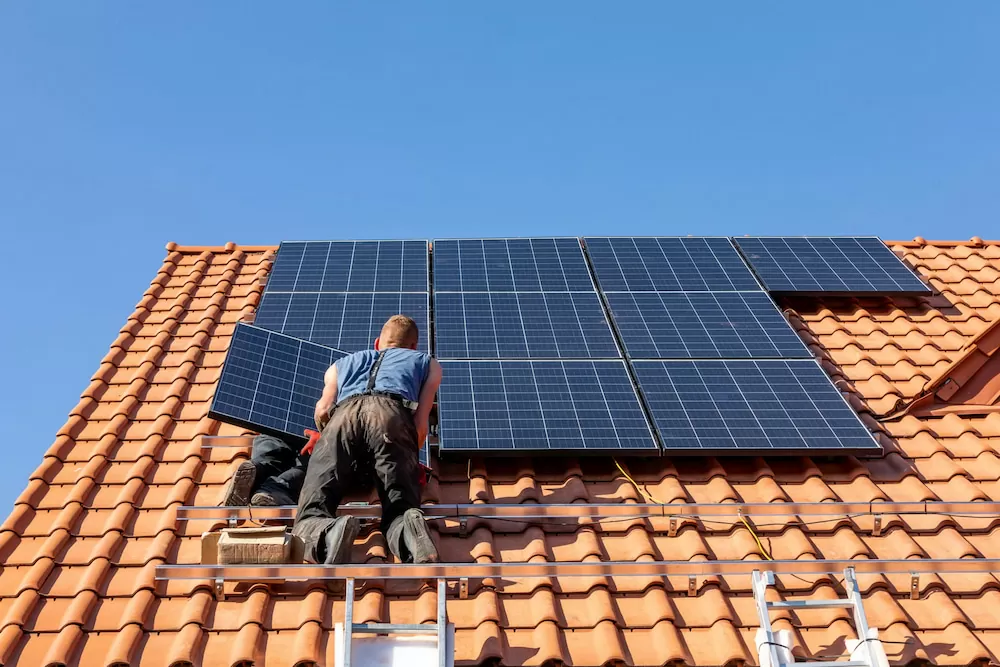 Workers installing solar electric panels on a house roof