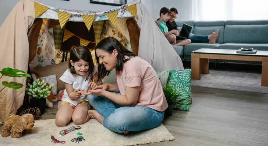 Mother and daughter play camping at home while father and son use laptop on the sofa