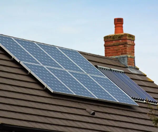 Solar panels installed on a tiled house roof beside a brick chimney, with a solar thermal panel visible nearby.