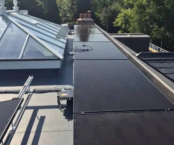Row of sleek black solar panels installed on a slate roof in Sussex with a garden view