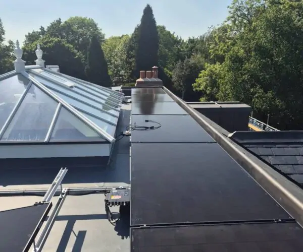 Rooftop view with a glass skylight, large black solar panels on a flat roof, and trees in the background.